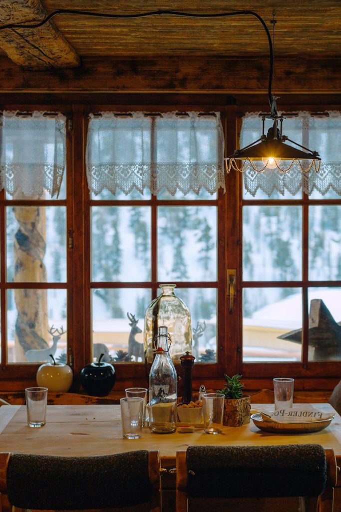 Interior of old wooden building with decor on table and windowsill against snowy trees in countryside
